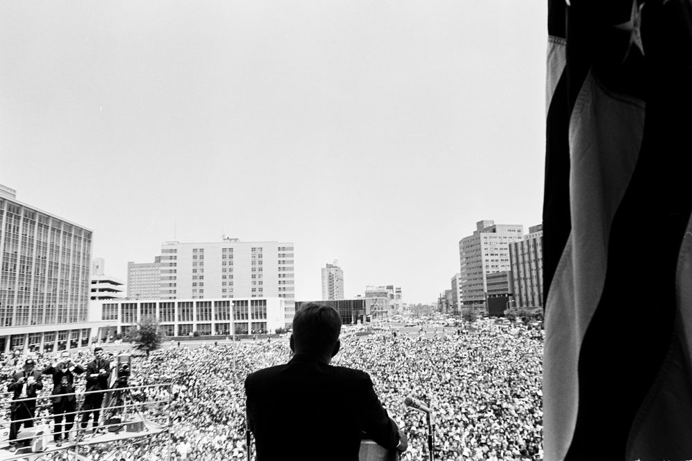 JFKWHP-ST-157-3-62. Black-and-white photograph of John F. Kennedy, with his back to the camera, addressing a large crowd before him.